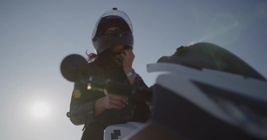 A motorcyclist takes off her helmet and gets off her bike in the desert