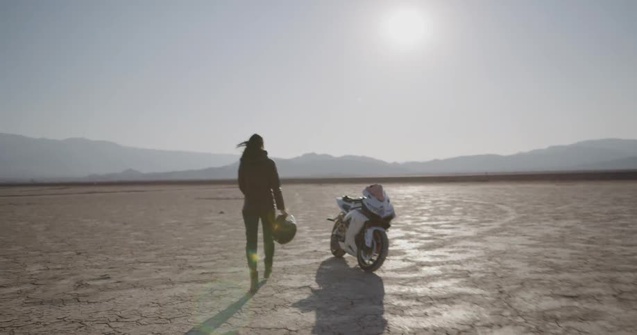 A woman walks towards her motorcycle and gets on it