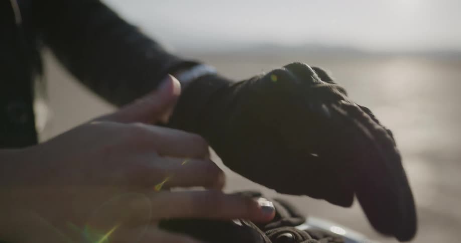 A person takes off motorcycle riding gloves and sets them on their motorcycle in the desert