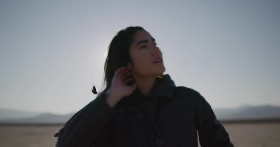 A woman runs her hand through her hair and holds a helmet as she walks away from her motorcycle in the desert
