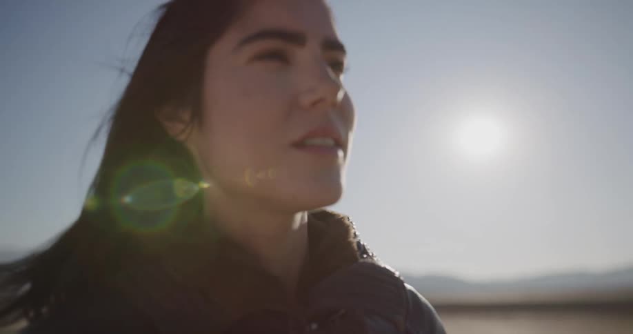 Female motorcyclist standing on the dry plain looks around and enjoys herself on a sunny day