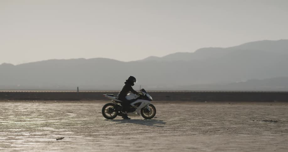 A person starts and begins to ride their motorcycle in the desert