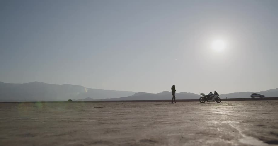 Woman puts on crash helmet and mounts motorcycle in desert at day
