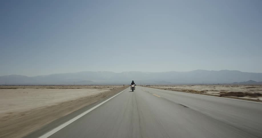 A person on a motorcycle traveling along a road through the desert