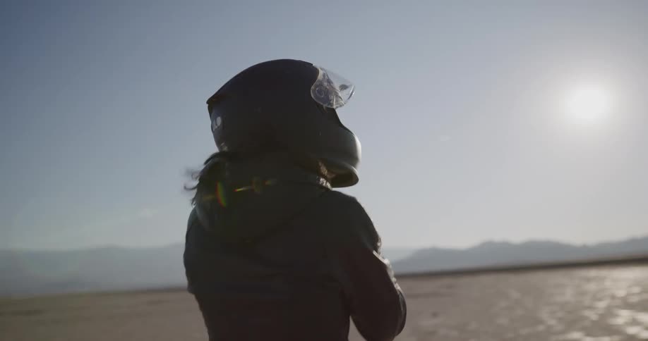 A woman walks in the desert towards her bike putting her helmet on as she walks