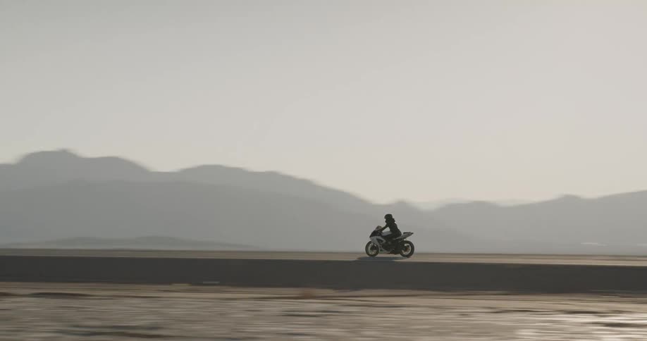 Motorcyclist rides along road between arid desert and fog shrouded mountains