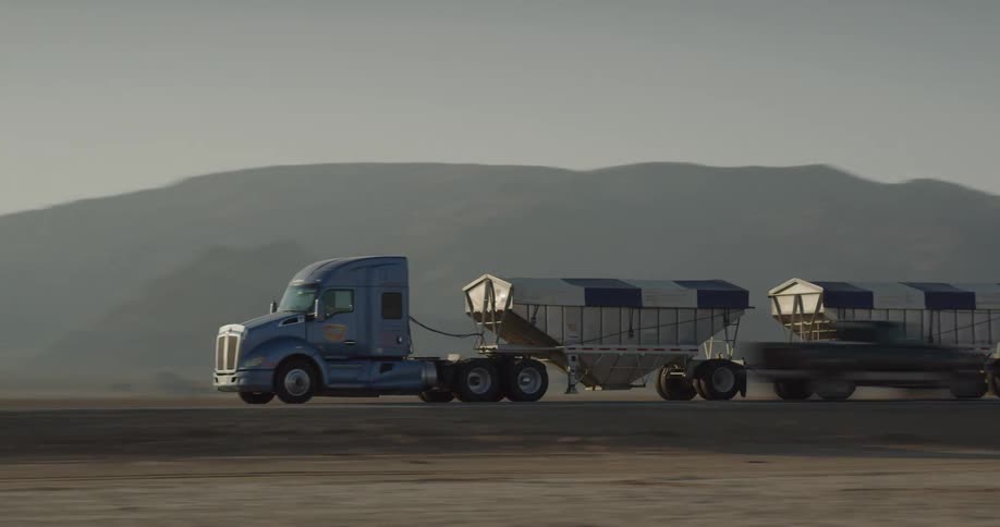 Two trucks hauling similar cargo pass each other going in opposite directions on a desert road