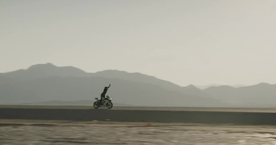 A woman stands up as she drives her motorcycle