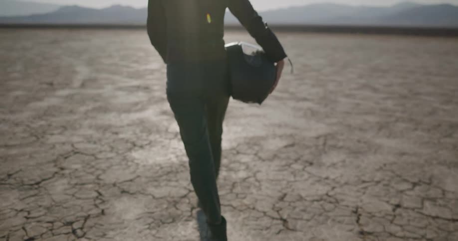 A woman carrying a helmet walks across the soil
