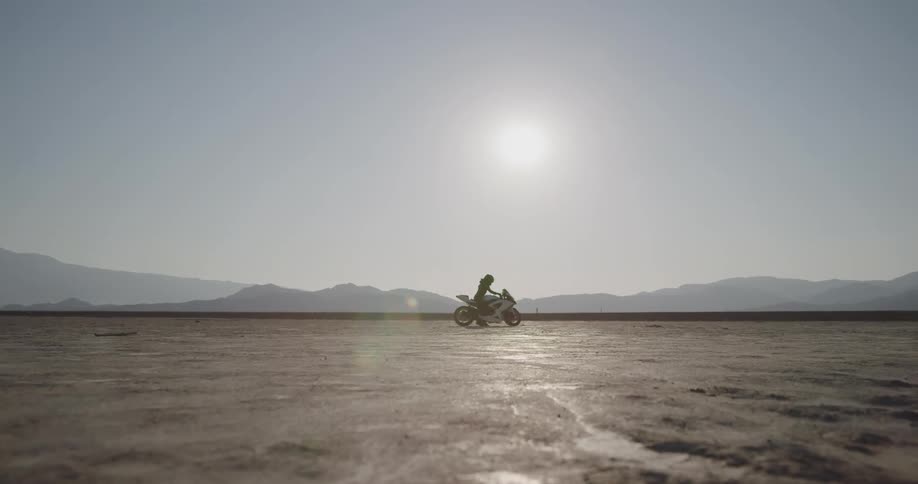 A person adjusting their glove and gripping the handles of a motorcycle in a desert