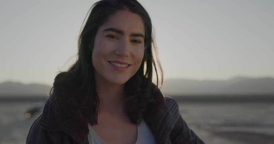 A woman in a leather jacket standing in the desert smiling into the camera