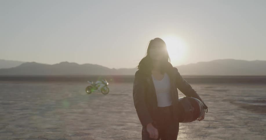 A woman dressed in leather removing her sunglasses with one hand while standing in a desert