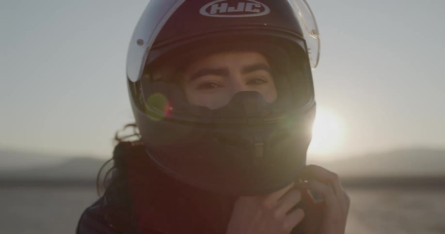 Woman puts helmet on and goes to motorcycle in desert at sunset