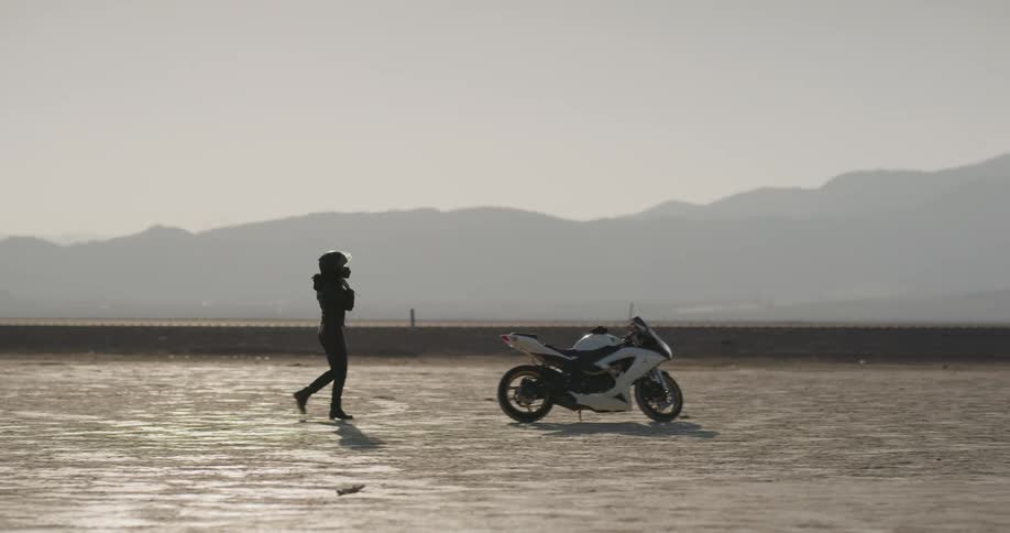 A woman puts her helmet on as she walks to her motorcycle and then gets on it