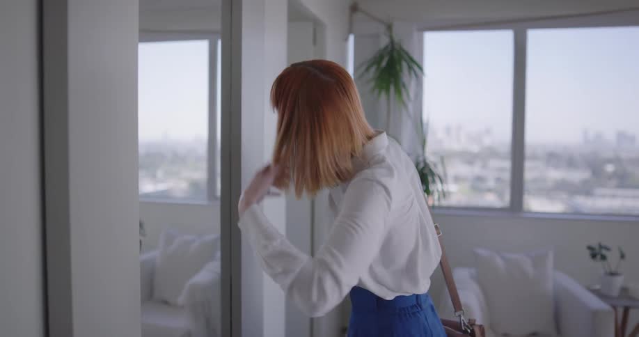 A woman looks in the mirror and fixes her hair before leaving the house