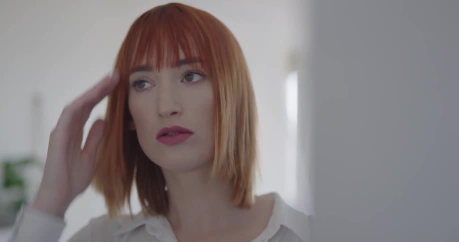 A woman approaching a mirror to adjust her hair before walking off
