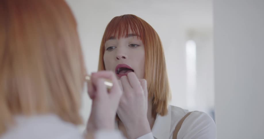 Woman applies lipstick while looking into mirror in home