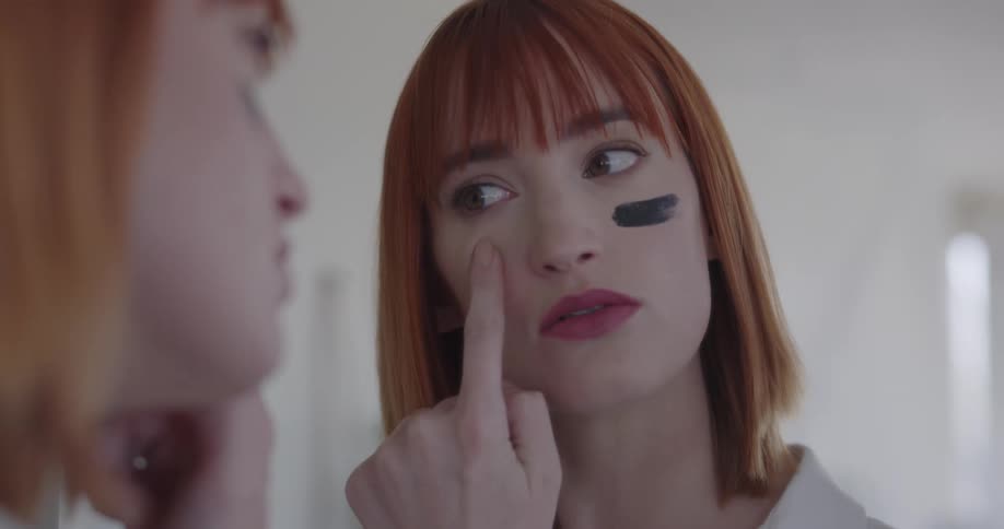 A woman putting black marks on her face with makeup