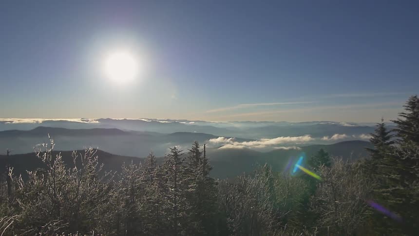 The sun shines over the mountain top and trees