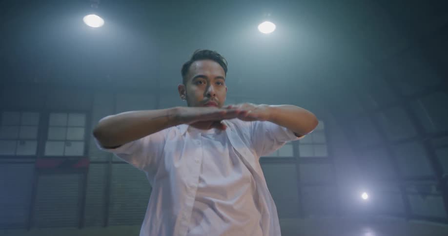 A man moves his arms while performing a modern dance in a large open space