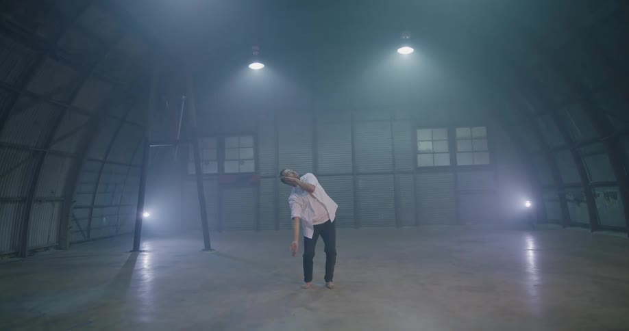 A man does a modern dance in a large open room