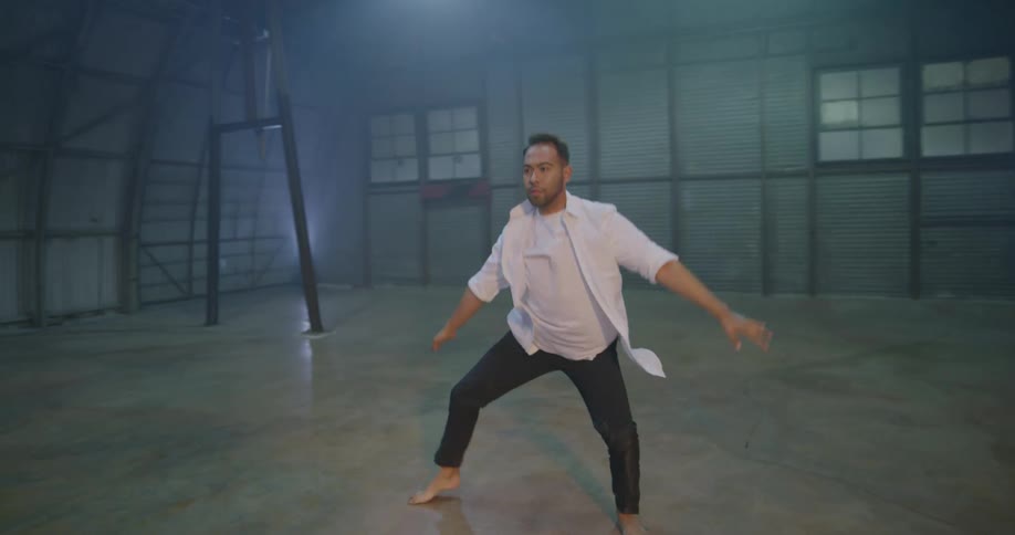 A man practices ballet dancing in an empty metal room