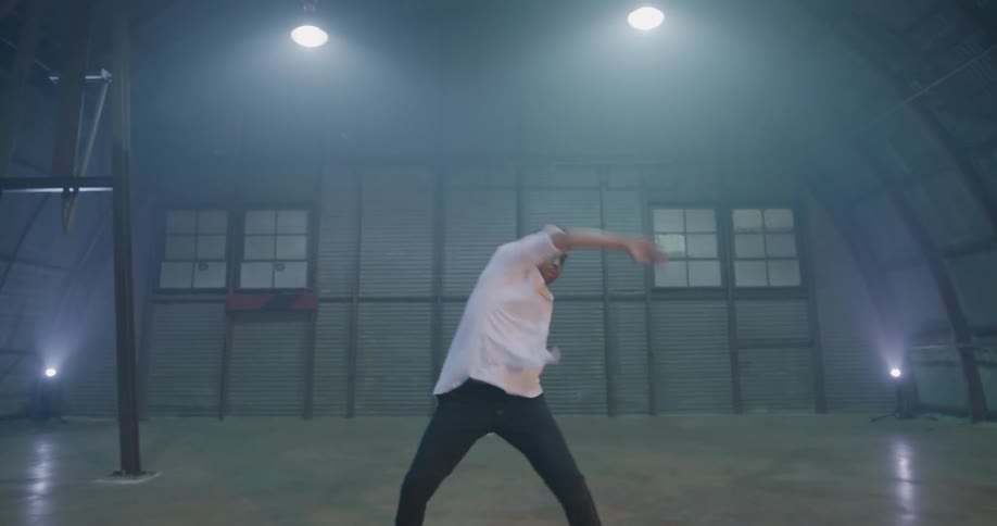 A man finishes a modern dance in a large open hangar
