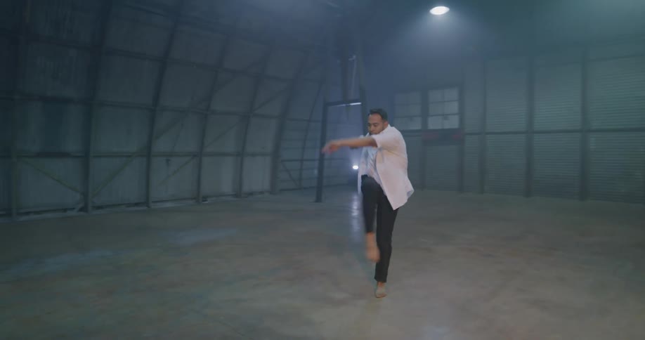 A man spins and poses while performing a modern dance in an empty hangar