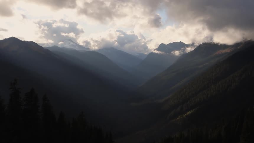 A cloud-covered mountain range with trees in the foreground