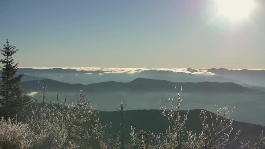 The sun shines on a cloud layer hovering over mountains