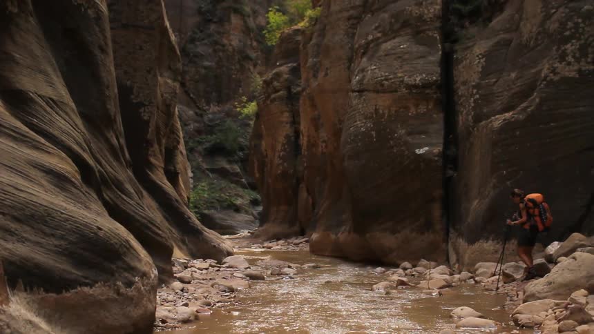 A man uses sticks to hike over a rocky river
