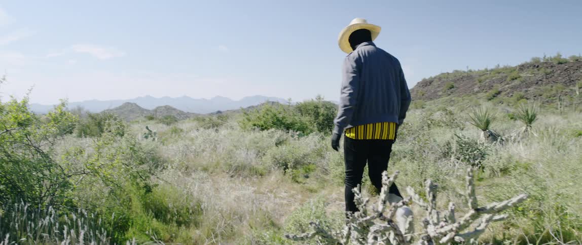 A man in a cowboy hat stepping over a shrub in the hills