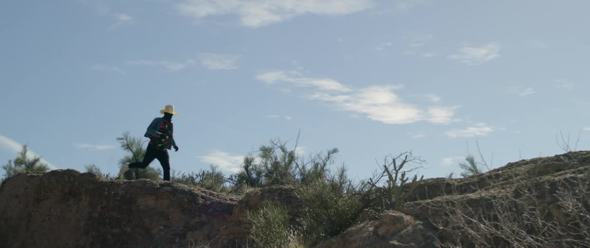 A man wearing a cowboy hat runs across a ranch
