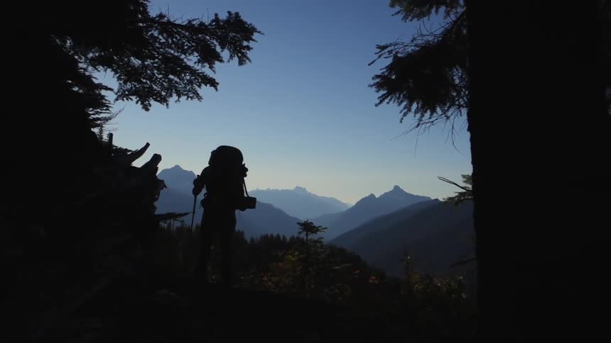 A hiker walking down a mountain trail that overlooks other mountain peaks