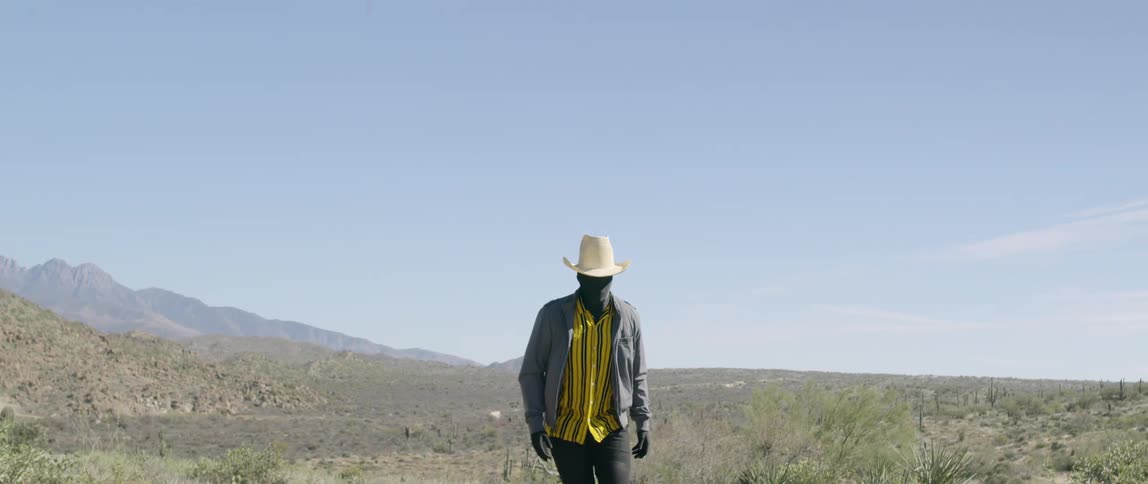 Cowboy walks across scrub covered plain with mountain in background