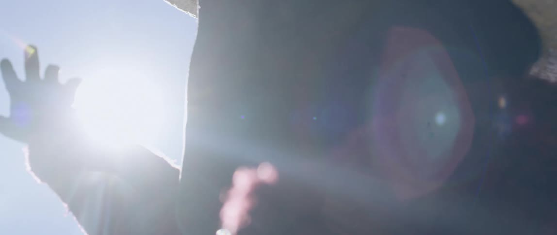 A young girl stands outside and reaches her arm out toward the sun