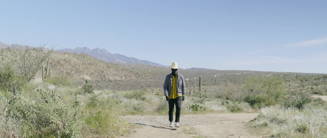 Man wearing cowboy hat walks on a path in dry plains