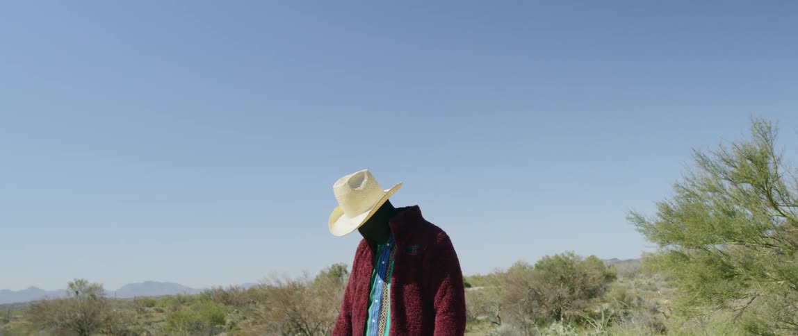A man wearing a black fabric that covers his skin under clothing lowering his arm while standing in a desert