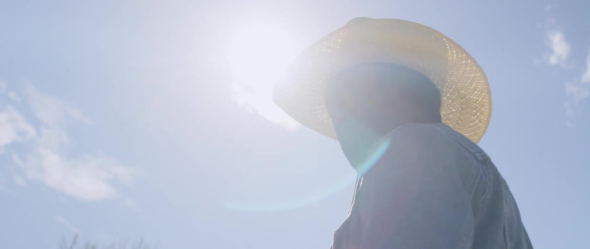 A black man in a straw cowboy hat standing outdoors on a sunny day