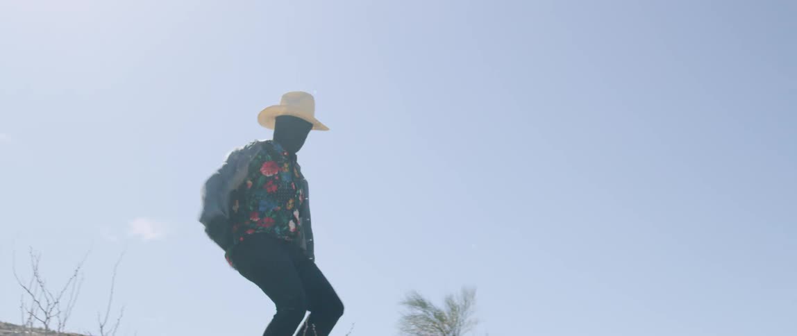 A man with black fabric covering his face running and jumping down a large rock