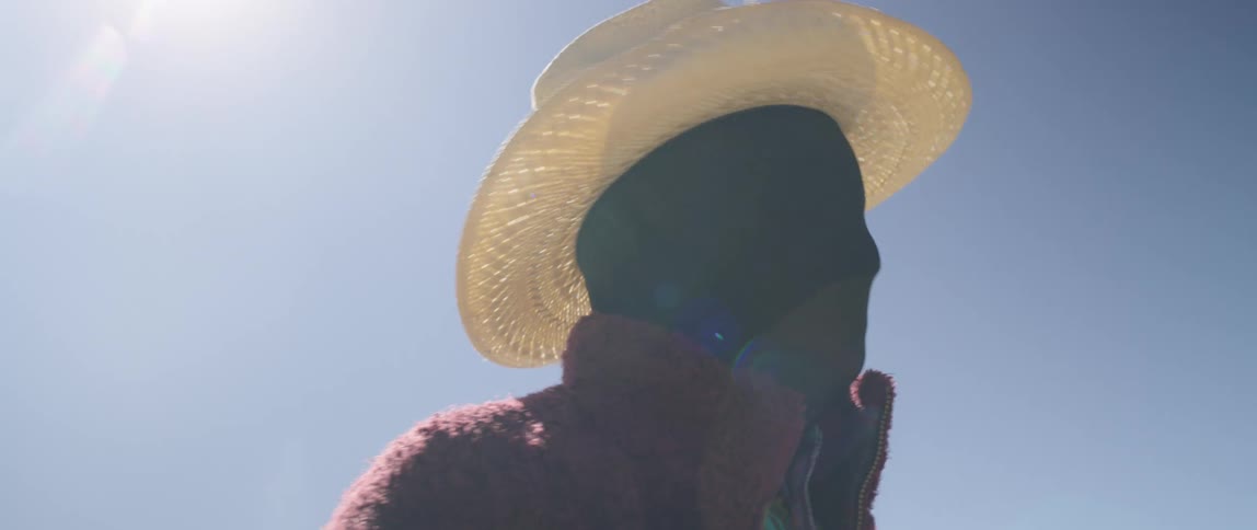 A man poses in a full facial covering and colorful clothing in a field