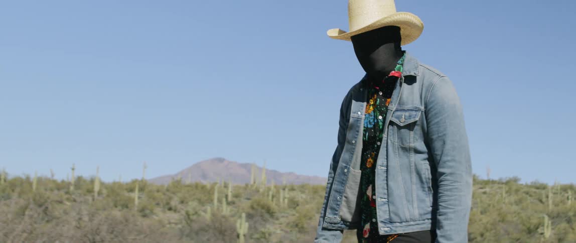A man wearing black fabric over his face walking through a field
