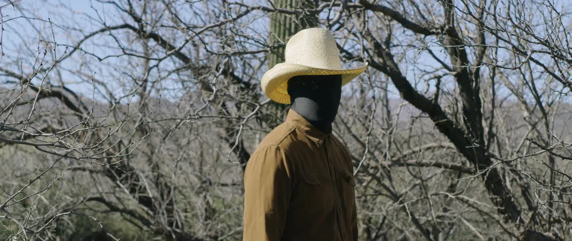 Cowboy wearing a black face mask turns around and looks at the camera on a hill