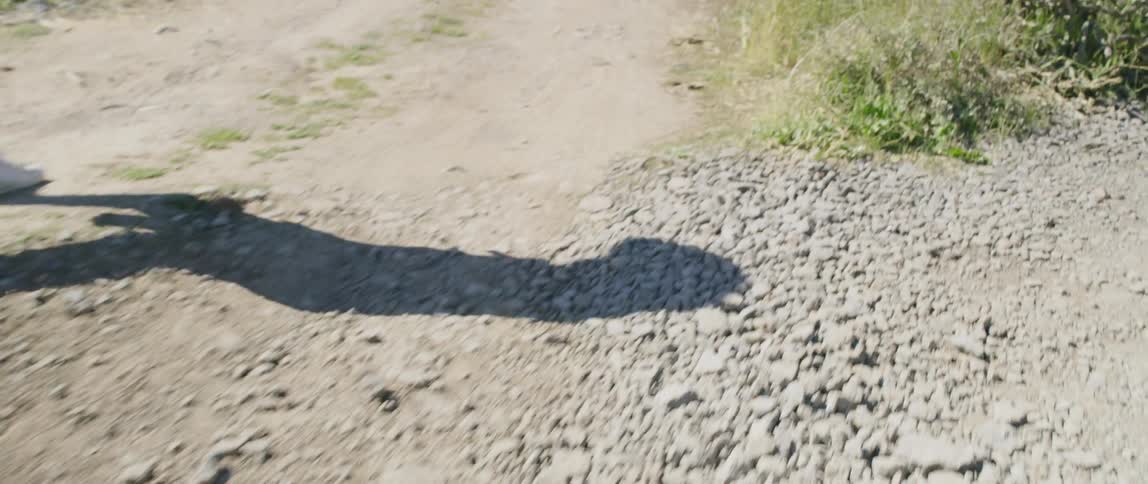 A mans shadow is projected onto nearby gravel as he walks alone down a dirt road