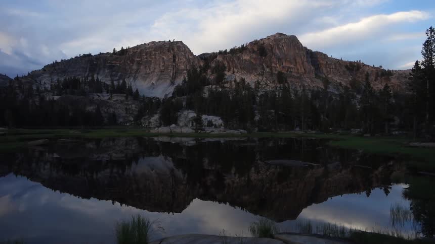 Mountains with trees reflecting in a body of water on a sunny day with clouds