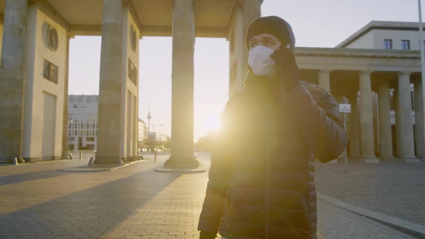 Man wearing face mask makes a phone call in empty plaza in front of government buildings