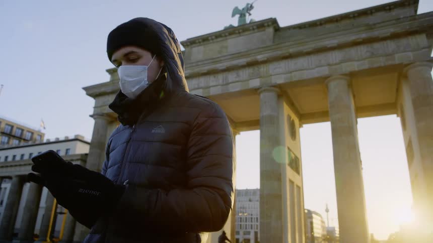 A man types on a smartphone while wearing a surgical mask