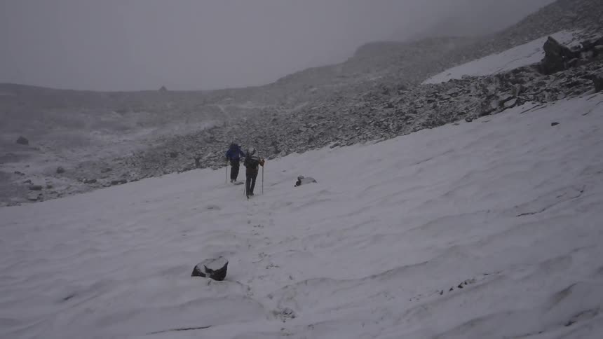 Two hikers travel up a snow covered slope on a snowy day