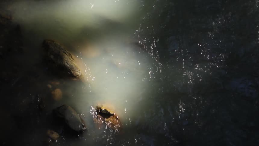 Water rippling and flowing around rock in dim lighting