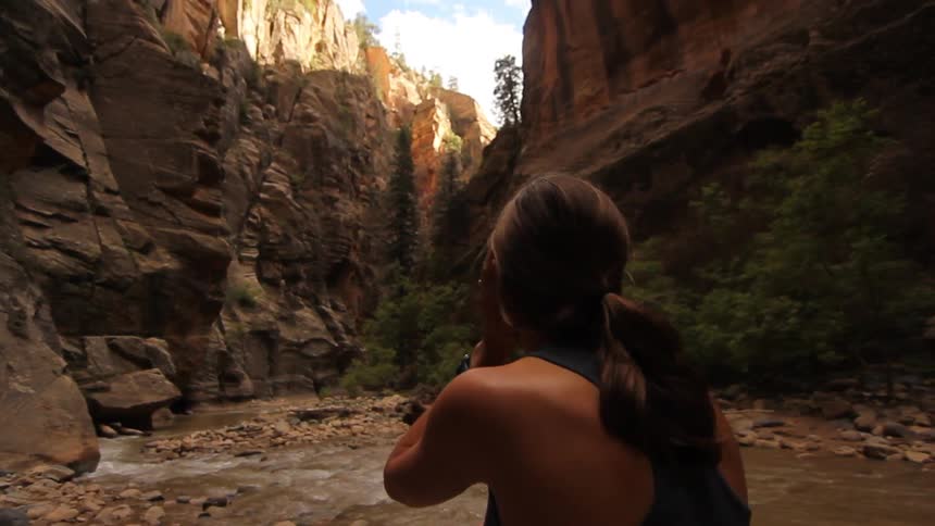 A woman standing in a canyon looks up at the rock walls